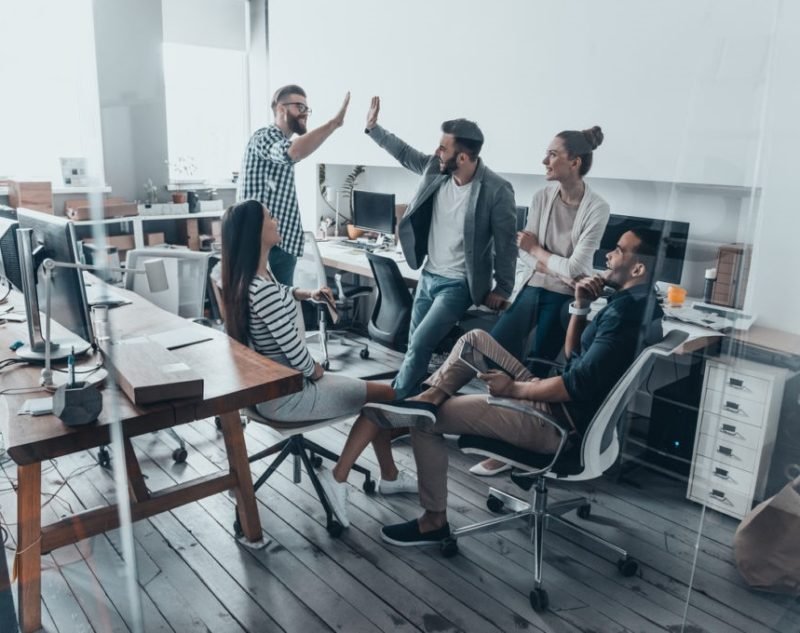 Two cheerful young business people giving high-five while their colleagues looking at them and smiling